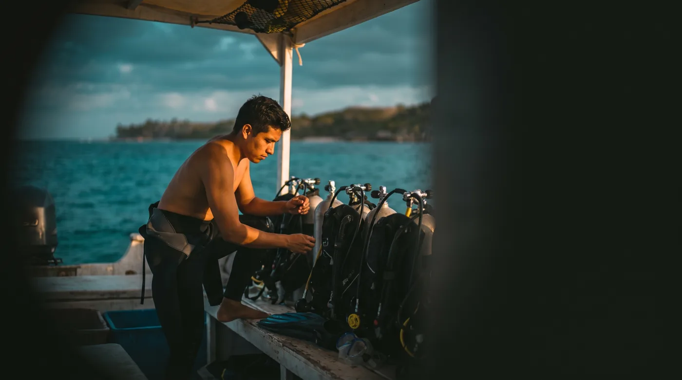 Un instructor de buceo revisa los tanques y el equipo alineados en la cubierta de una lancha pequeña, al amanecer, frente a la costa del Caribe.